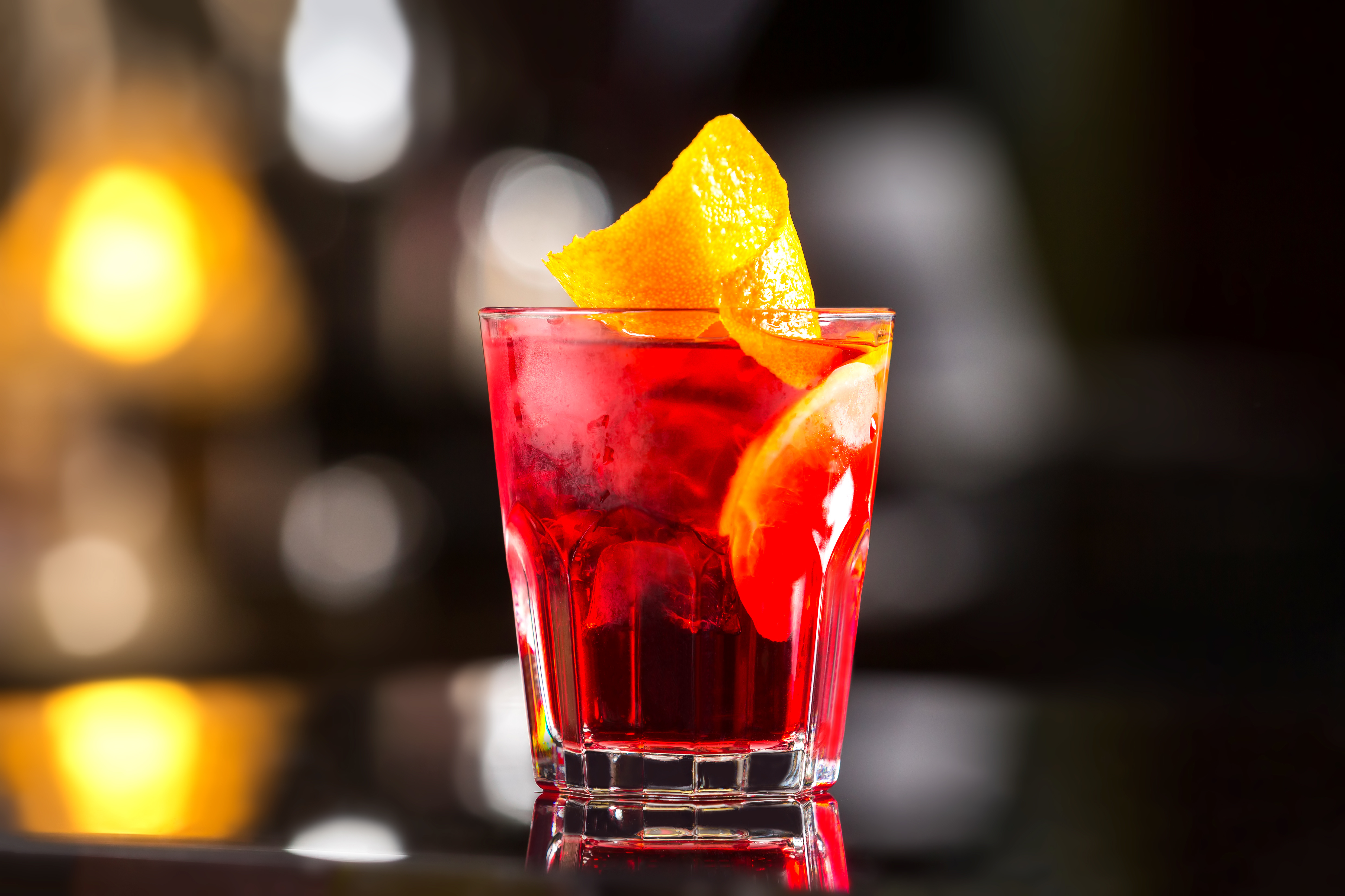 Closeup glass od red alcoholic cocktail decorated with lemon at bright bar stand background.