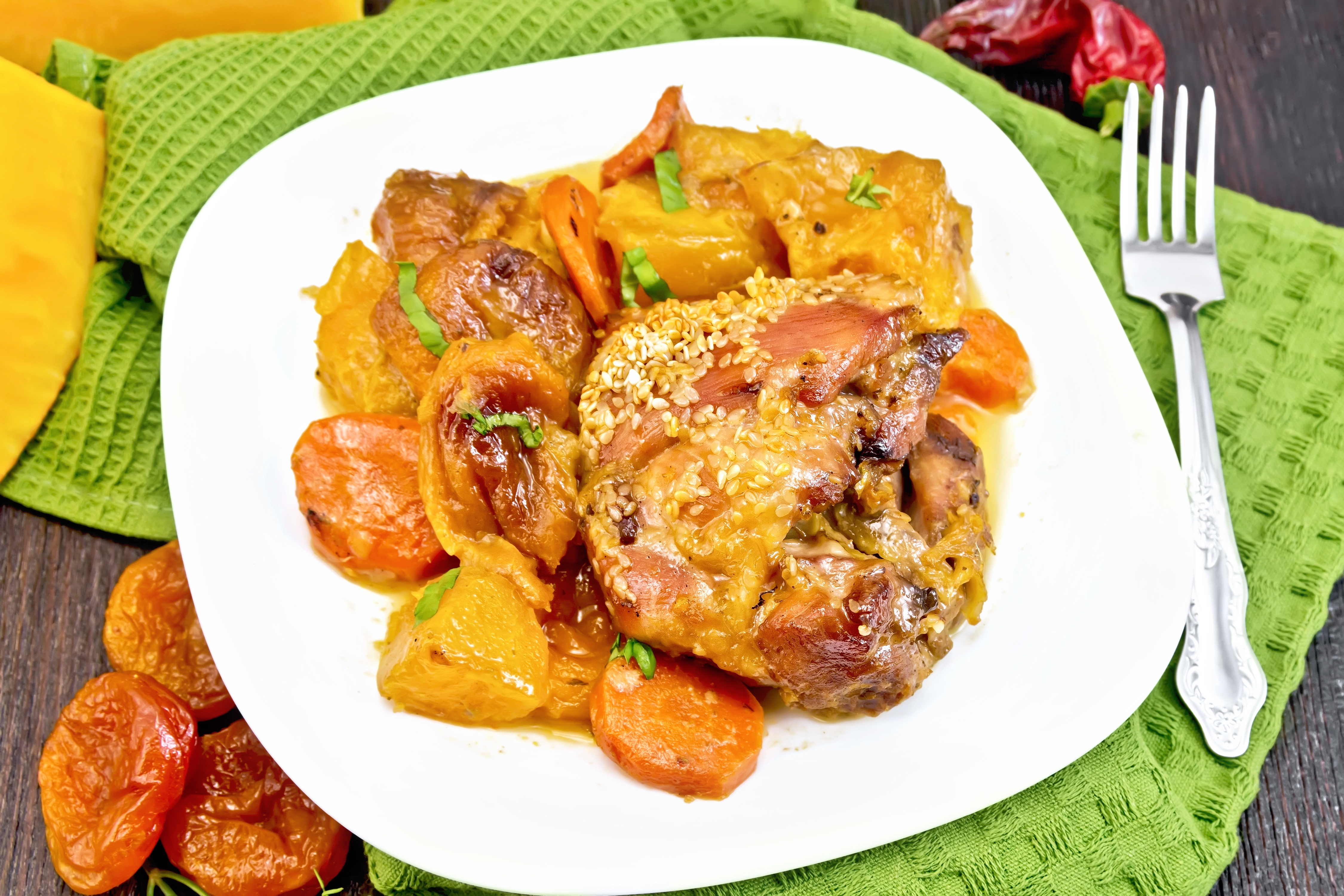 Chicken stew with pumpkin, dried apricots, carrots and red wine, sprinkled with sesame seeds in a plate on green napkin against dark wooden board