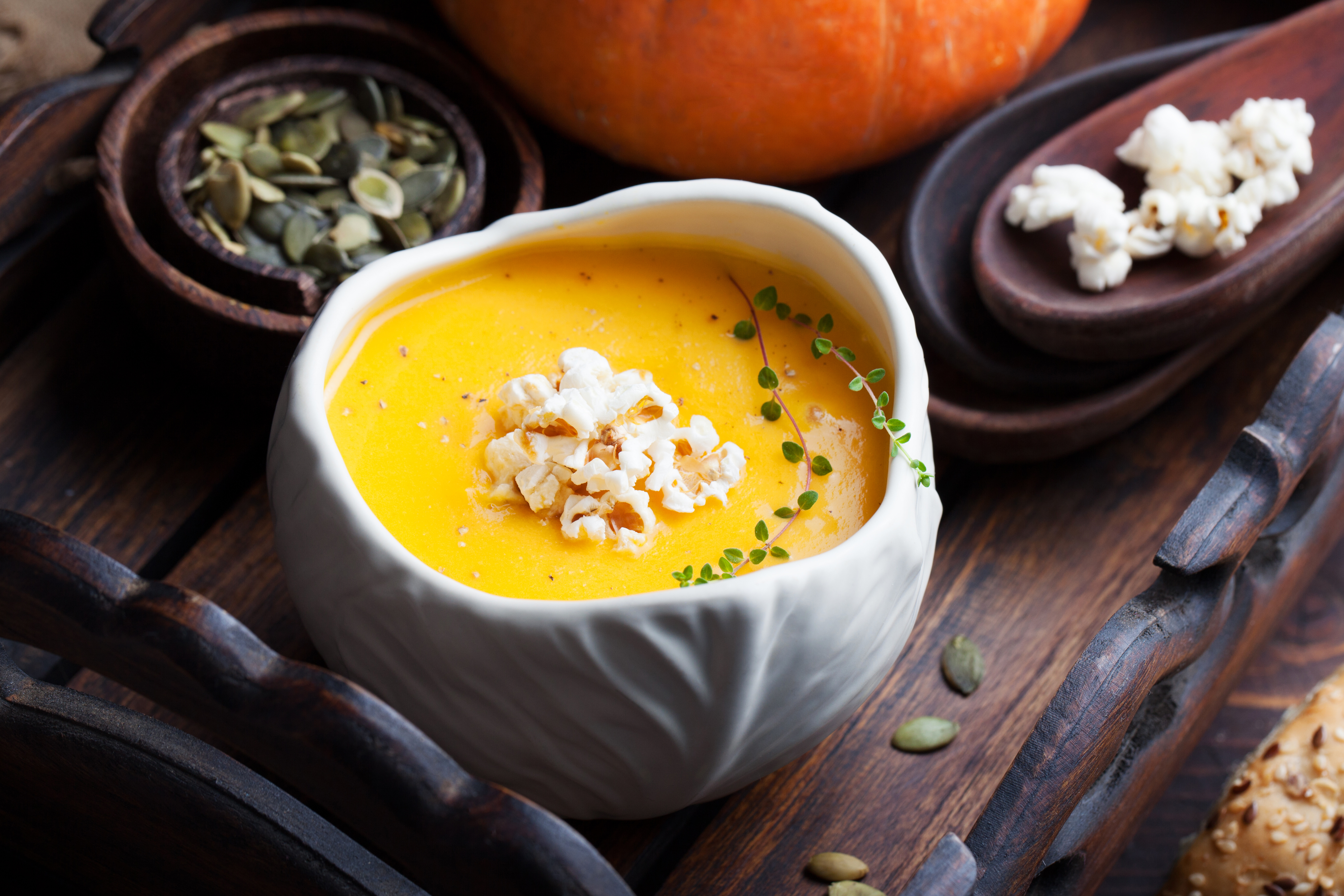 Pumpkin soup with salty popcorn in a white ceramic bowl with fresh pumpkin on a wooden background Top view